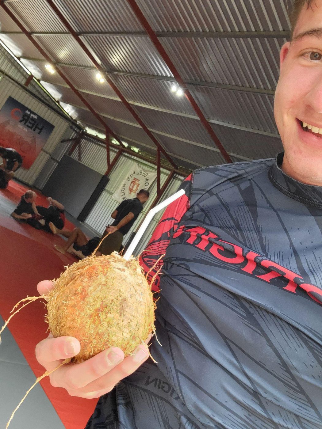 Duncan Bannon in a rash guard holding a fresh coconut at a jiu-jitsu gym in Costa Rica.