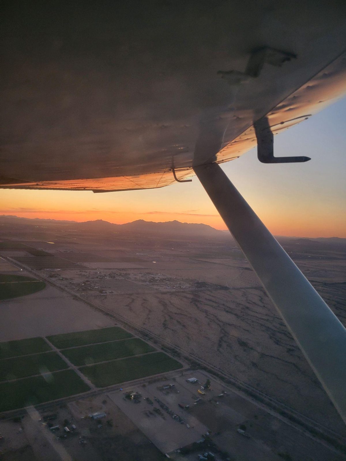 Arizona desert at sunset seen past the strut and wing of a light aircraft.